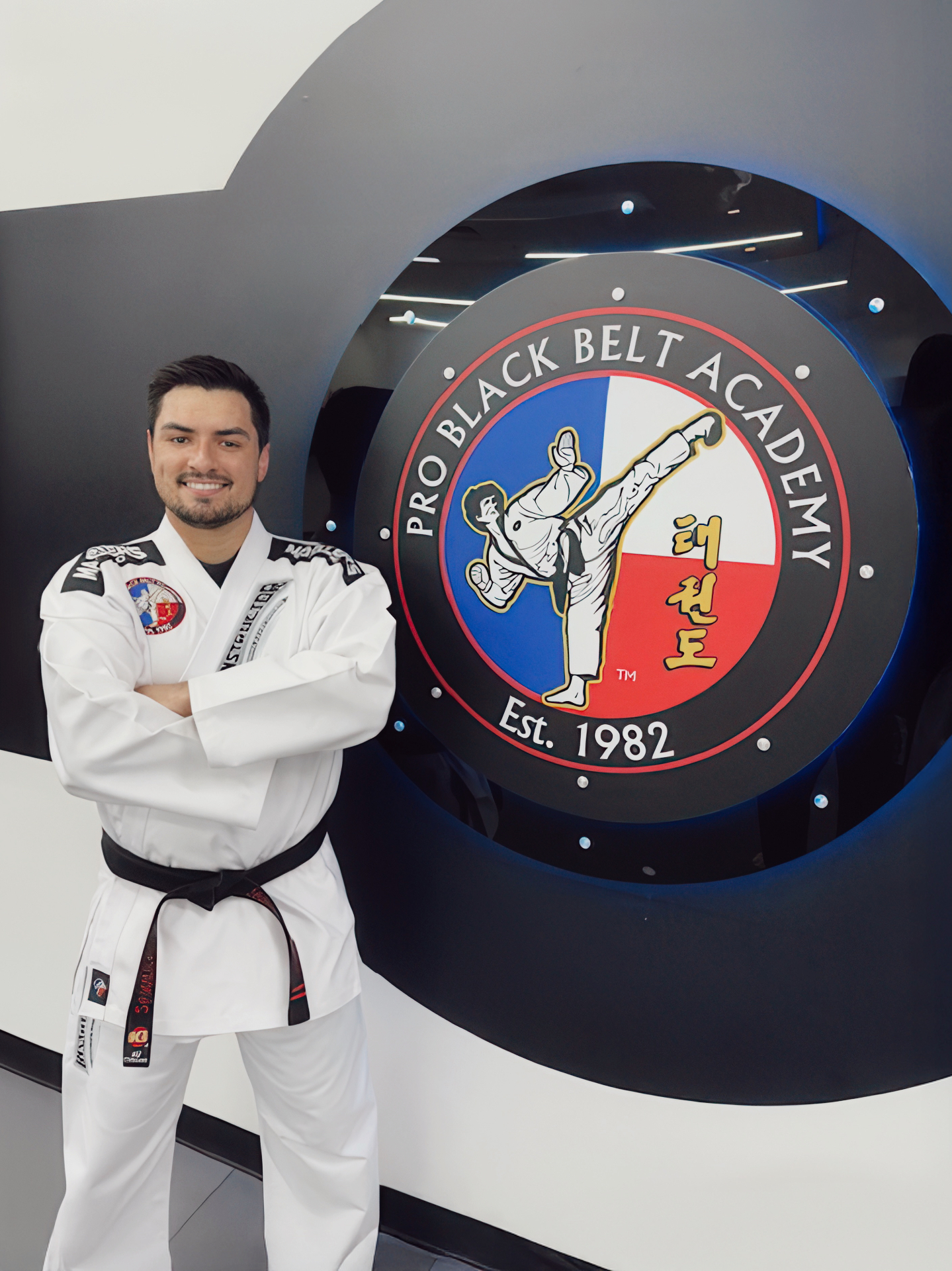 Instructor at Pro Black Belt Academy in front of the academy crest